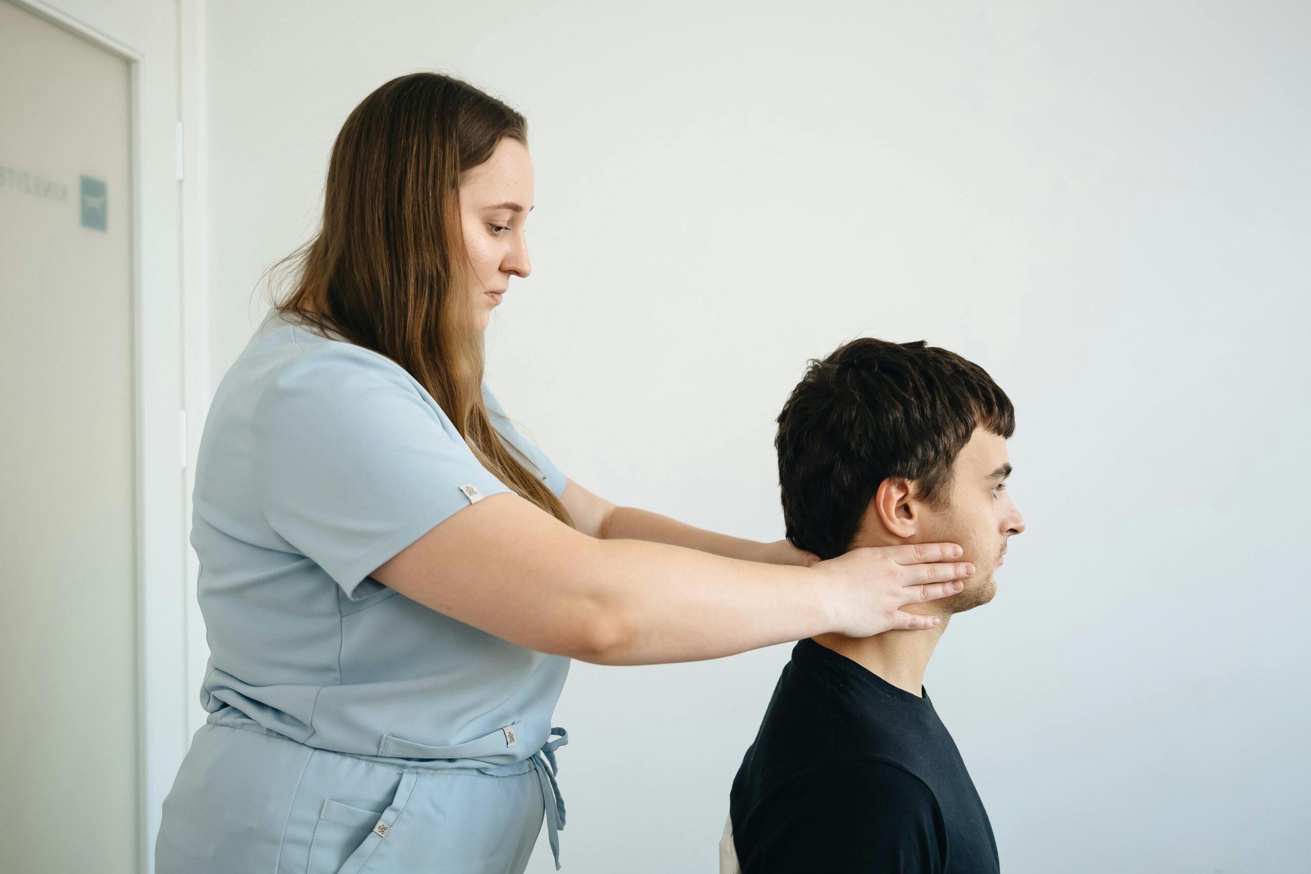 Home A physiotherapist performs a neck adjustment on a male patient in a clinic setting.