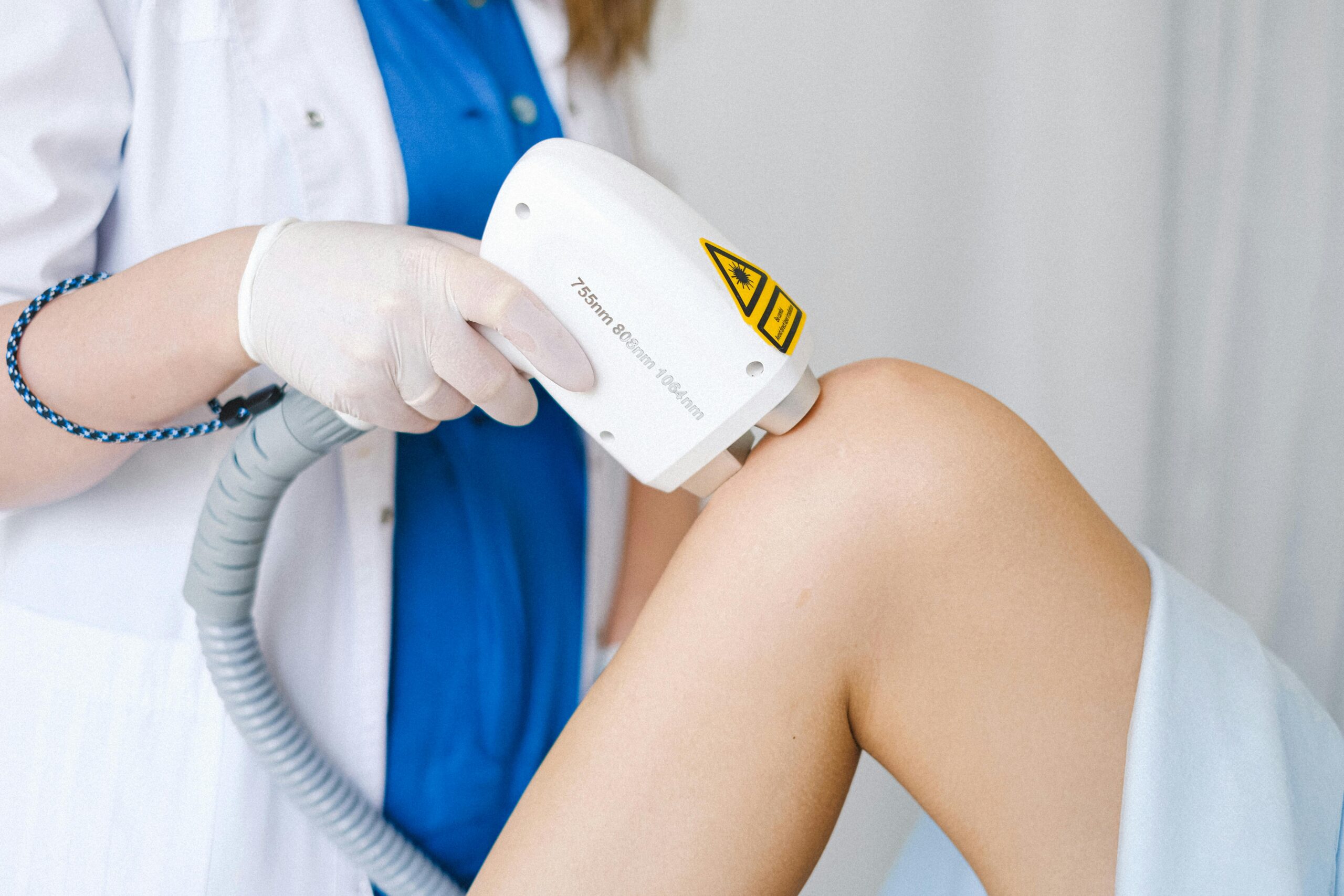 Home Crop unrecognizable cosmetologist in medical uniform using probe while doing low level laser therapy to calm patient in beauty salon
